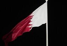 Qatar’s national flag waving against a dark night sky. The maroon-and-white flag is mounted on a tall pole.