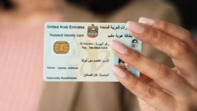 A hand holding a United Arab Emirates Resident Identity Card with the name "Isemty Urvatova" and nationality "Kazakhstan," featuring an ID number and a photo.