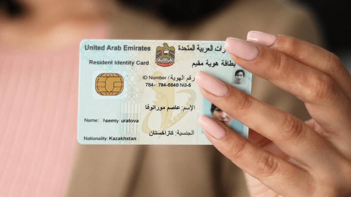 A hand holding a United Arab Emirates Resident Identity Card with the name 