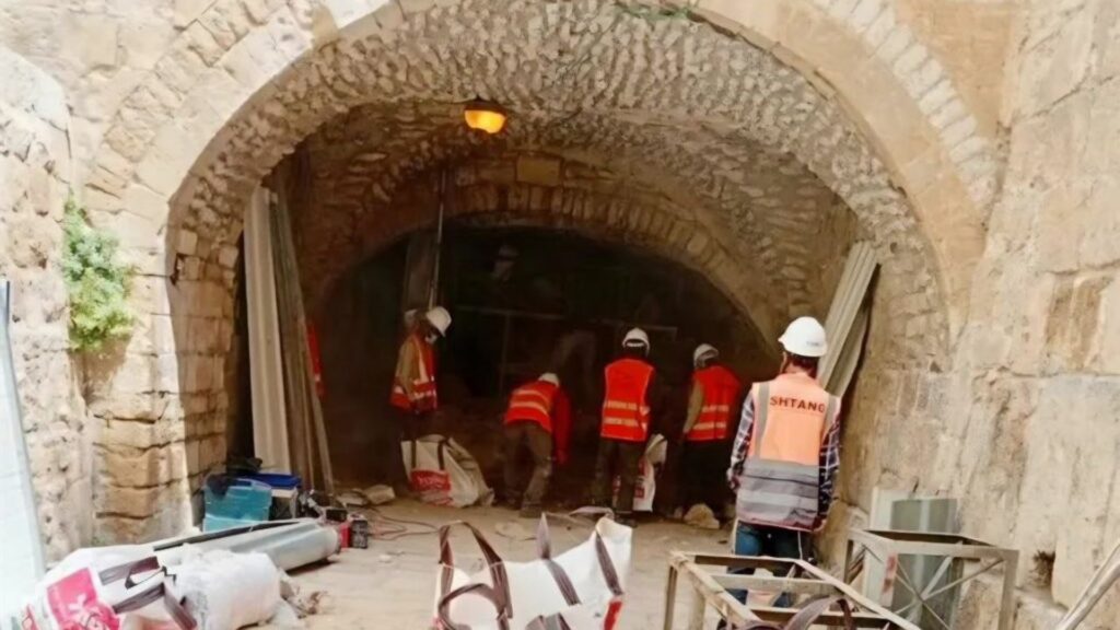 Workers in safety vests and helmets carrying out excavation under an old stone archway.