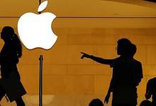 Silhouettes of people outside an Apple store with a glowing Apple logo.