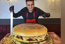 Celebrity chef CZN Burak smiles while posing with a giant burger and fries at his restaurant.