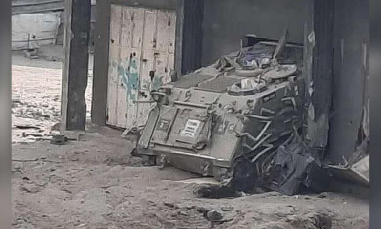 Booby-trapped armoured vehicle sits abandoned near a concrete building in Gaza City, surrounded by rubble and sand.