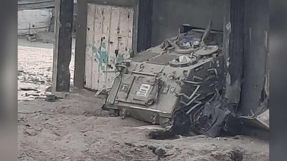 Booby-trapped armoured vehicle sits abandoned near a concrete building in Gaza City, surrounded by rubble and sand.