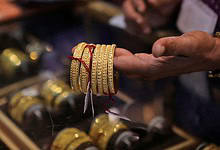 A person holding several intricately designed gold bangles in a jewellery shop, with more bangles displayed in a glass case below.