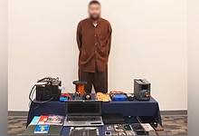 A suspect stands in front of security evidence, including electronic devices and materials seized by Kuwaiti police.