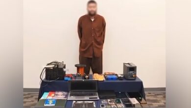 A suspect stands in front of security evidence, including electronic devices and materials seized by Kuwaiti police.