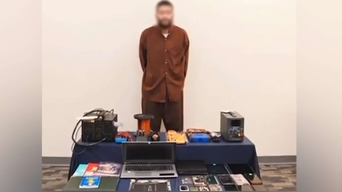 A suspect stands in front of security evidence, including electronic devices and materials seized by Kuwaiti police.