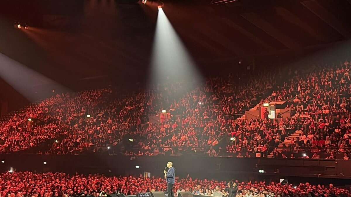 Mehdi Hasan speaking on stage at Wembley Arena during a Gaza fundraiser event, with a large audience in the background.