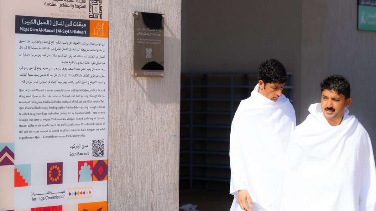Pilgrims at Miqat Qarn Al-Manazil preparing to enter Ihram, with informational signage provided by the Royal Commission for Makkah City and Holy Sites.