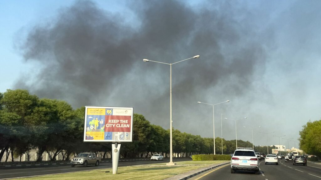 Black smoke rises above trees and a busy road in Doha following reported explosions.