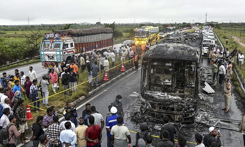 Police personnel and others gather near a Bengaluru-bound private bus that caught fire after colliding with a two-wheeler, with the blaze being triggered after the motor bike with its fuel cap open was dragged underneath the bus in Kurnool district on Friday. At least 20 people were killed in the accident. (PTI Photo)