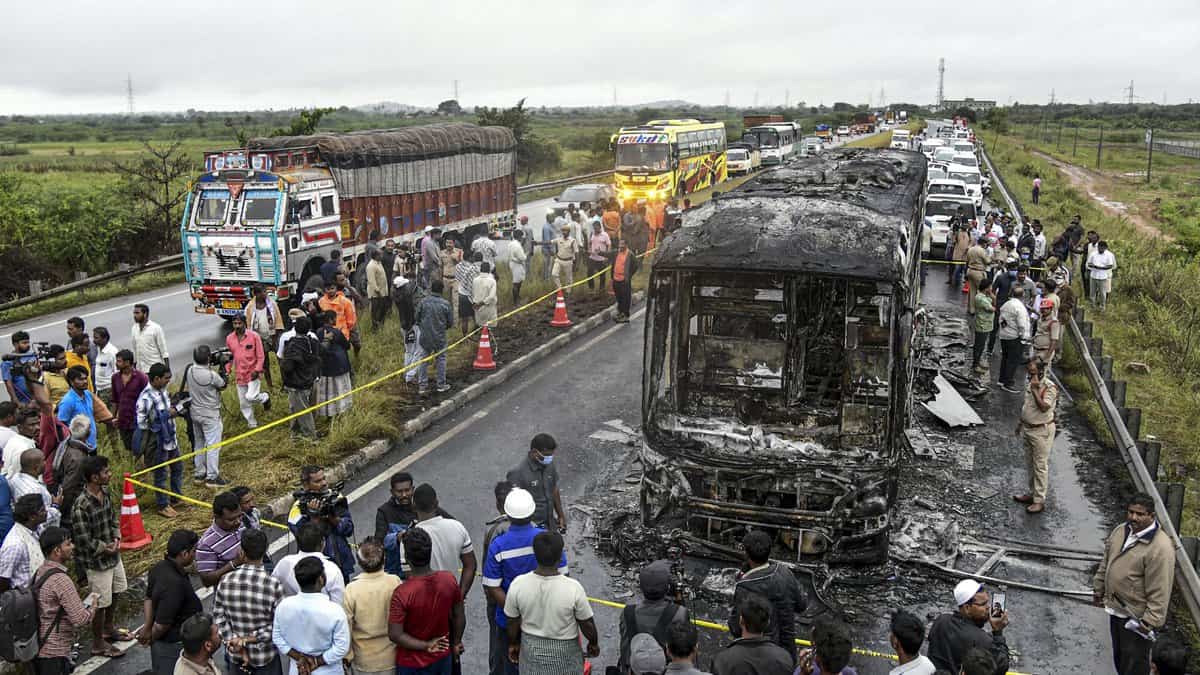 Police personnel and others gather near a Bengaluru-bound private bus that caught fire after colliding with a two-wheeler, with the blaze being triggered after the motor bike with its fuel cap open was dragged underneath the bus in Kurnool district on Friday. At least 20 people were killed in the accident. (PTI Photo)