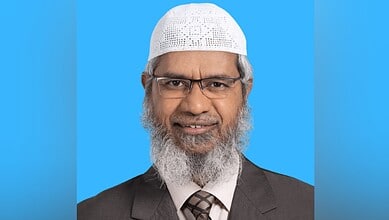 Zakir Naik pictured in a suit and white cap against a blue background.