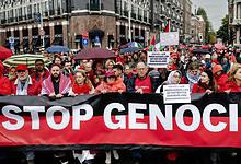 Protesters in Amsterdam wearing red hold a large banner reading “Stop Genocide” during a mass rally in solidarity with Gaza.