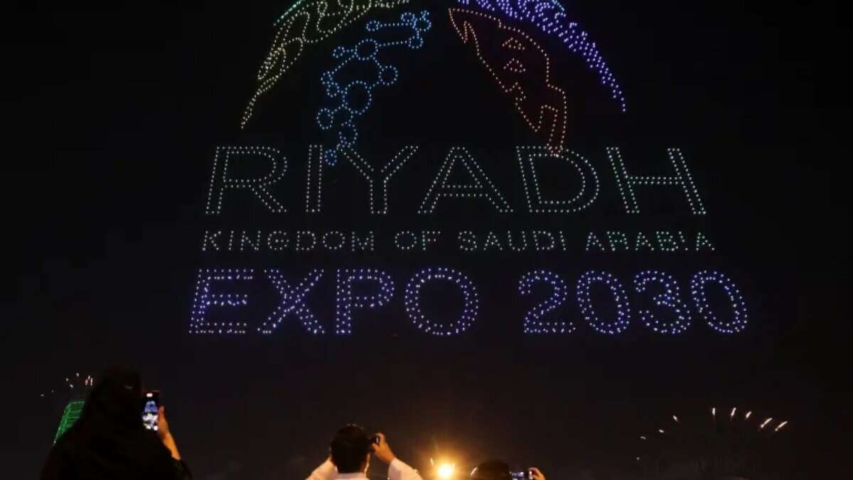 People photograph a night sky drone display forming the “Riyadh Expo 2030” logo during celebrations in Saudi Arabia.
