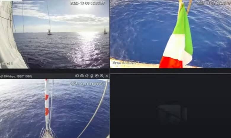 A live stream from the Freedom Flotilla shows several vessels sailing across the calm Mediterranean Sea under clear skies. One boat flies the Italian flag as sunlight reflects on the water’s surface.