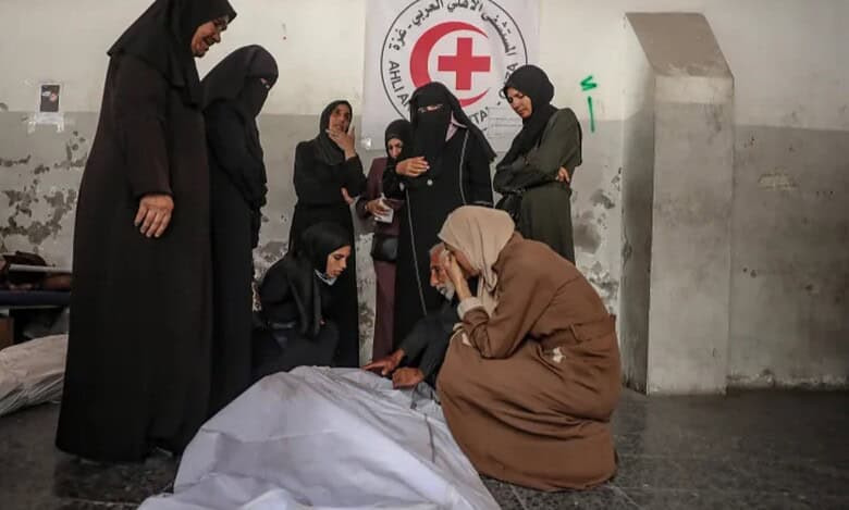 Palestinian family mourns beside bodies wrapped in white shrouds inside a hospital in Gaza.