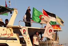 Activists aboard a Gaza-bound flotilla boat wave Algerian and Palestinian flags, with one person raising a peace sign and another holding a banner supporting Gaza
