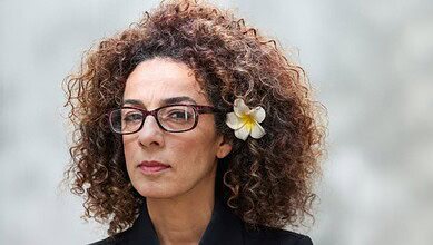 Iranian-American journalist Masih Alinejad wearing glasses and a flower in her hair, looking ahead against a neutral background.