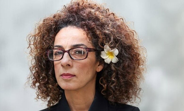 Iranian-American journalist Masih Alinejad wearing glasses and a flower in her hair, looking ahead against a neutral background.