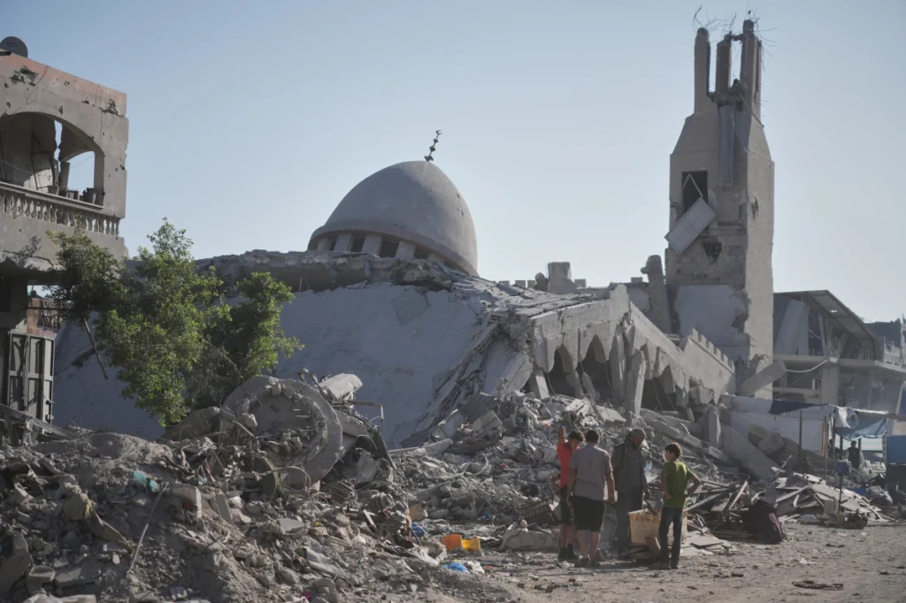 Palestinians walk through the rubble of destroyed buildings and a damaged mosque in Gaza City following recent attacks.