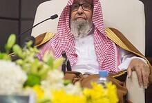 Sheikh Saleh Al-Fawzan seated during an official event, wearing a traditional Saudi robe and red-and-white ghutra.