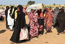 Displaced Sudanese civilians carry belongings through a camp in El Fasher.