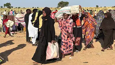 Displaced Sudanese civilians carry belongings through a camp in El Fasher.