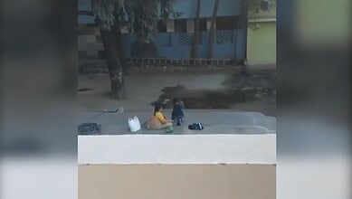 Image shows a woman dressing a young girl in a compound