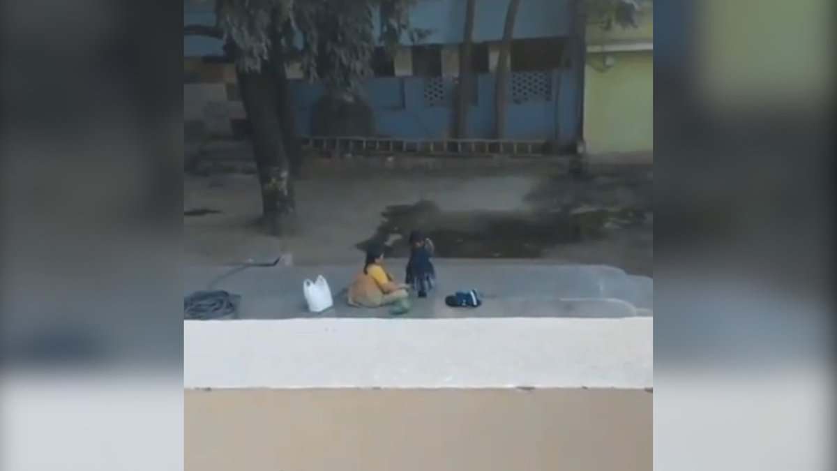 Image shows a woman dressing a young girl in a compound