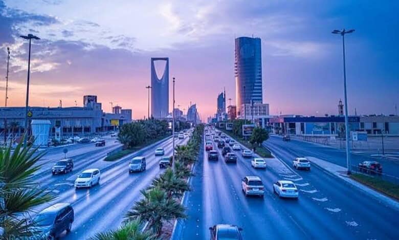 Evening view of a busy highway in Riyadh with the Kingdom Tower and modern skyscrapers under a colourful sky.