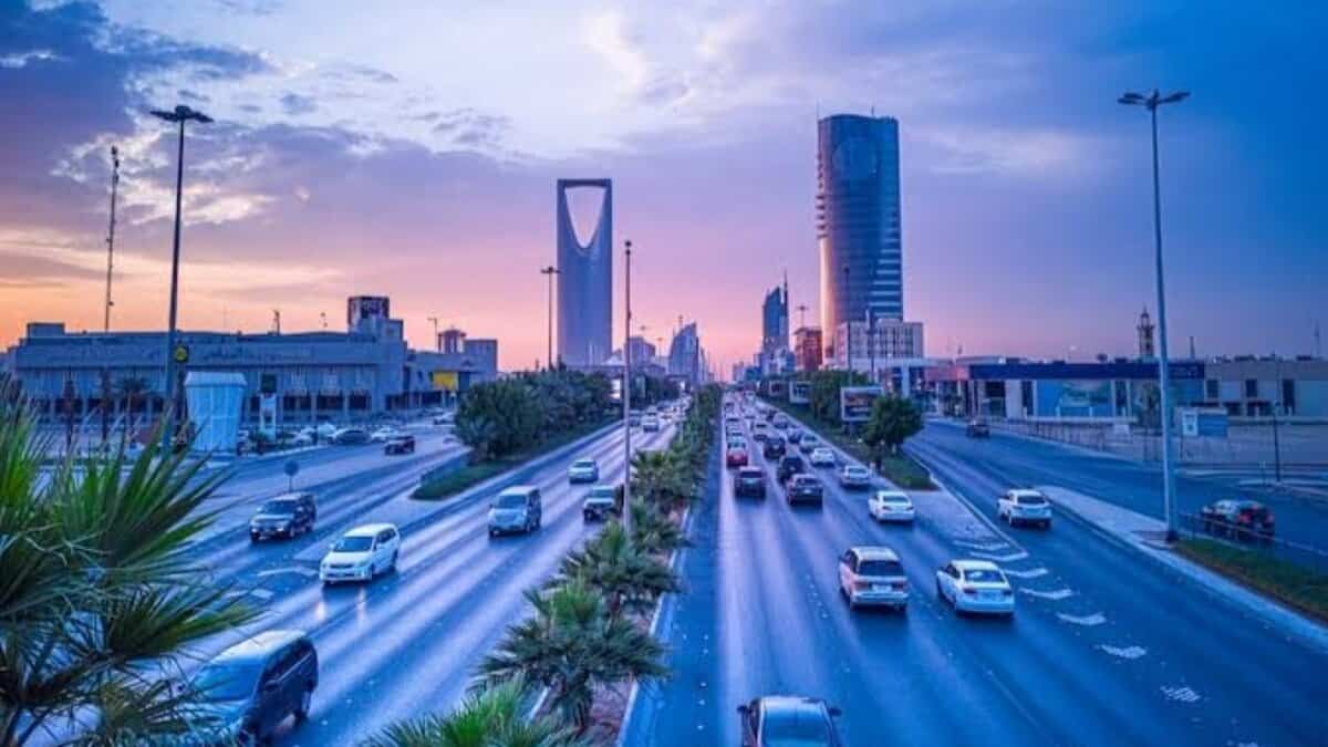 Evening view of a busy highway in Riyadh with the Kingdom Tower and modern skyscrapers under a colourful sky.