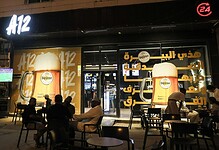 Night view of A12 Cafe in Riyadh with customers seated outside and large posters advertising Warsteiner 0.0 percent alcohol-free beer on the storefront.