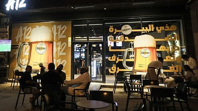 Night view of A12 Cafe in Riyadh with customers seated outside and large posters advertising Warsteiner 0.0 percent alcohol-free beer on the storefront.