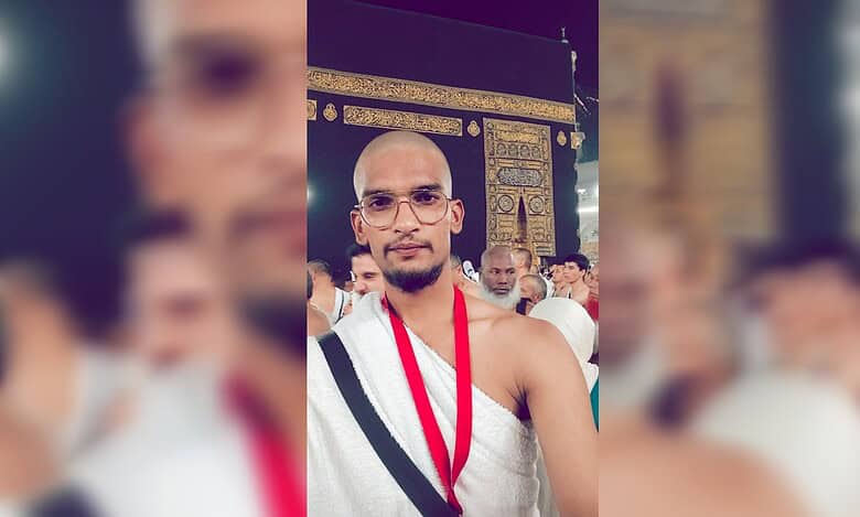 Abdul Shoeb Mohammed standing in front of the Kaaba during Umrah, wearing ihram and glasses, with pilgrims in the background.