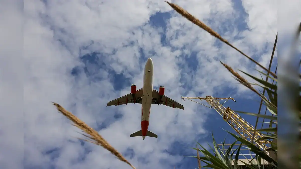 Airbus A320 flying overhead against a partly cloudy sky.
