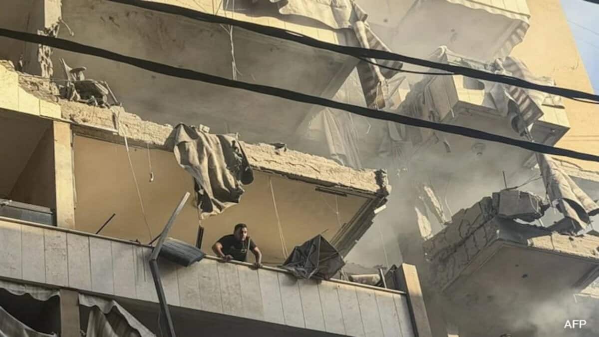 A damaged Beirut building after an Israeli airstrike, with a man standing on a shattered balcony.