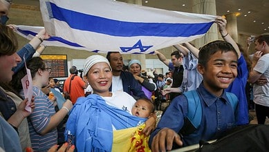 Bnei Menashe families from India arrive at Ben Gurion Airport, smiling and holding an Israeli flag.