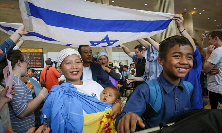Bnei Menashe families from India arrive at Ben Gurion Airport, smiling and holding an Israeli flag.