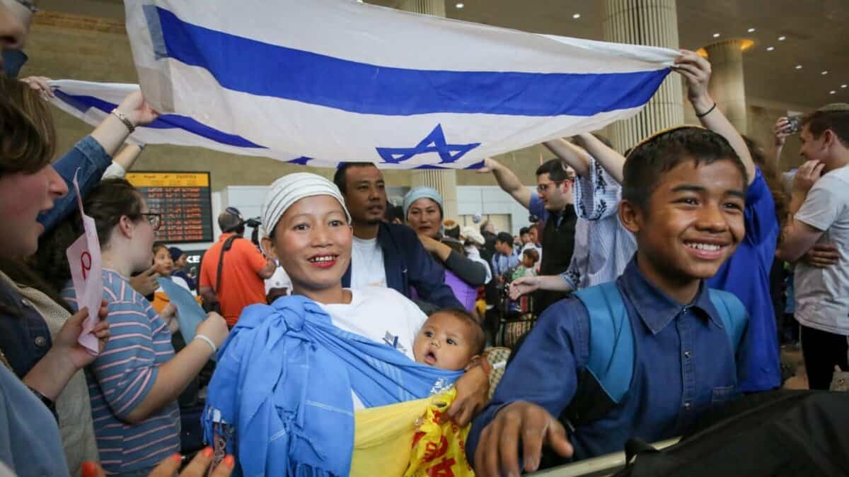 Bnei Menashe families from India arrive at Ben Gurion Airport, smiling and holding an Israeli flag.