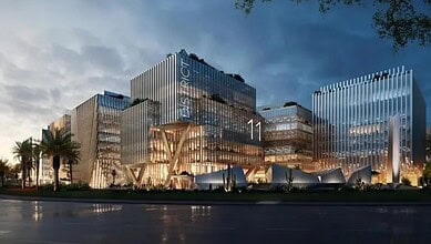 View of Al Marwan’s District 11 smart work resort in Sharjah, featuring modern glass buildings illuminated with warm lighting.