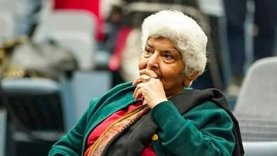 Dr Arfa Sayeda Zehra seated during an event, wearing a green shawl and red outfit, appearing thoughtful and composed.