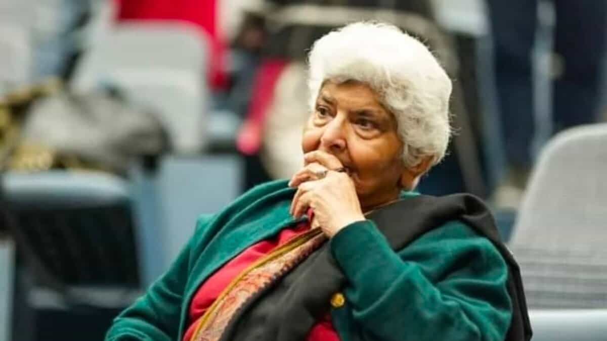 Dr Arfa Sayeda Zehra seated during an event, wearing a green shawl and red outfit, appearing thoughtful and composed.