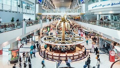 Representative image showing travellers moving through a busy terminal at Dubai International Airport, with the golden palm at the centre of the duty-free area.