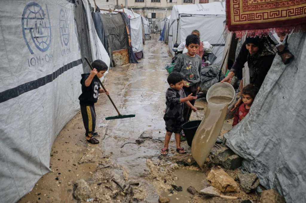 Children drain floodwater from between tents in a muddy Gaza camp.