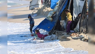 Children near makeshift tents as waves reach shelters on Gaza beach.