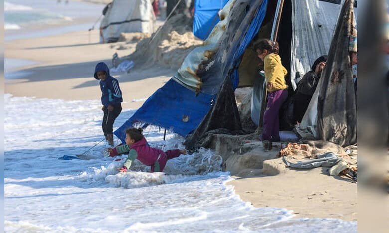 Children near makeshift tents as waves reach shelters on Gaza beach.