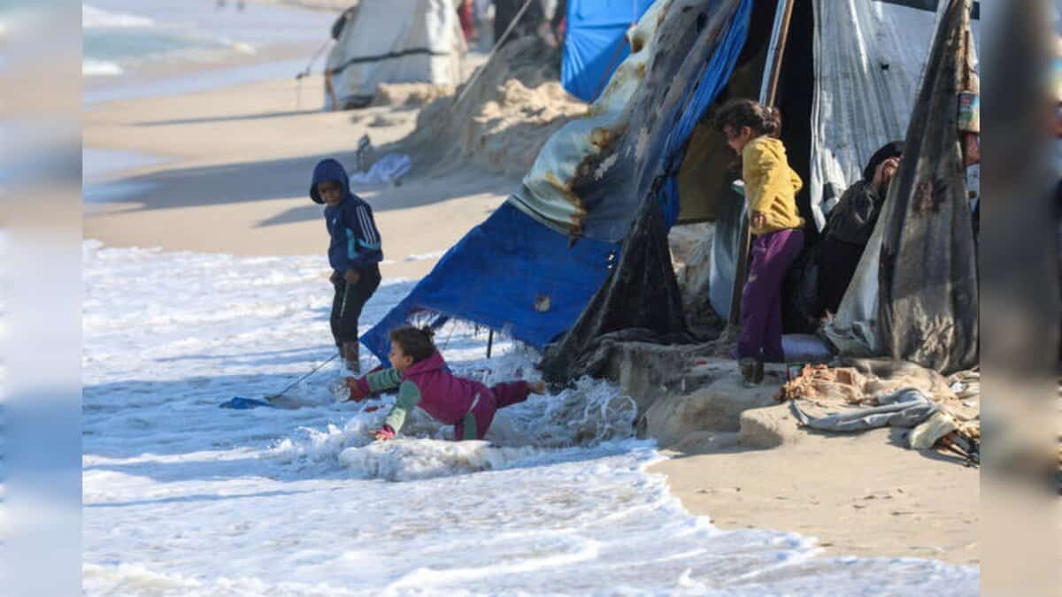Children near makeshift tents as waves reach shelters on Gaza beach.