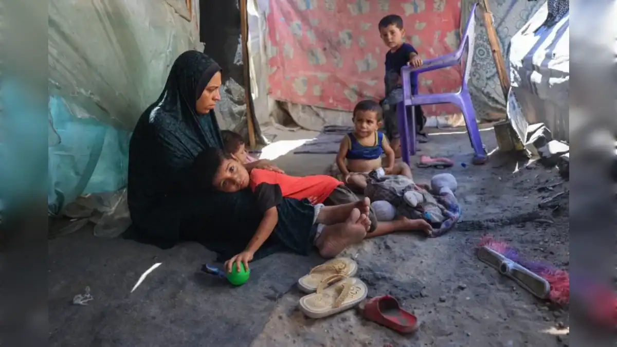 A mother sits with her young children inside a makeshift displacement shelter in Deir al-Balah during the hunger crisis in Gaza.